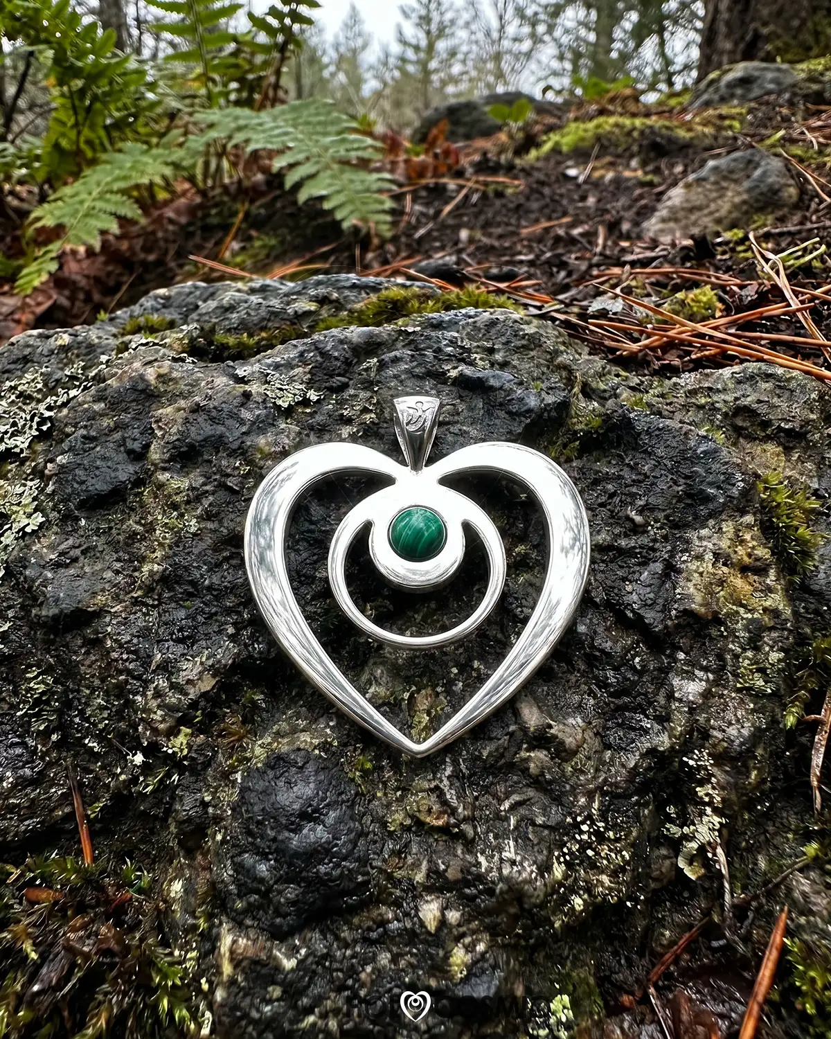 Holocosmic Colgante HoloCosmic en plata y malaquita tumbado en una roca. Joyeria energética de Iván-Holocosmic.